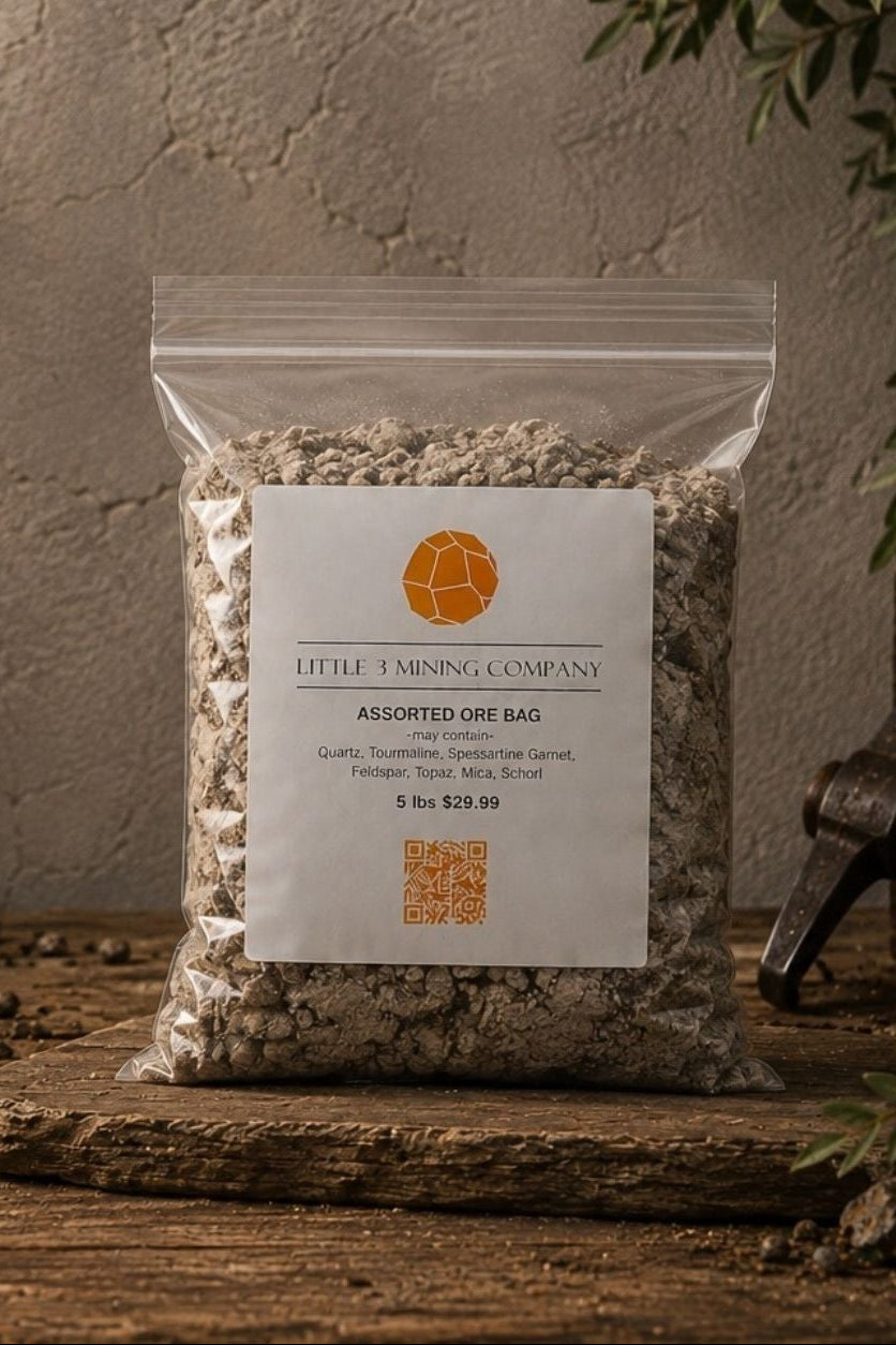 A clear plastic bag of Little Timed Company Assorted Fine Ball clay potting medium, standing on a rustic wooden surface with rocks, soil, and greenery in a styled setting.